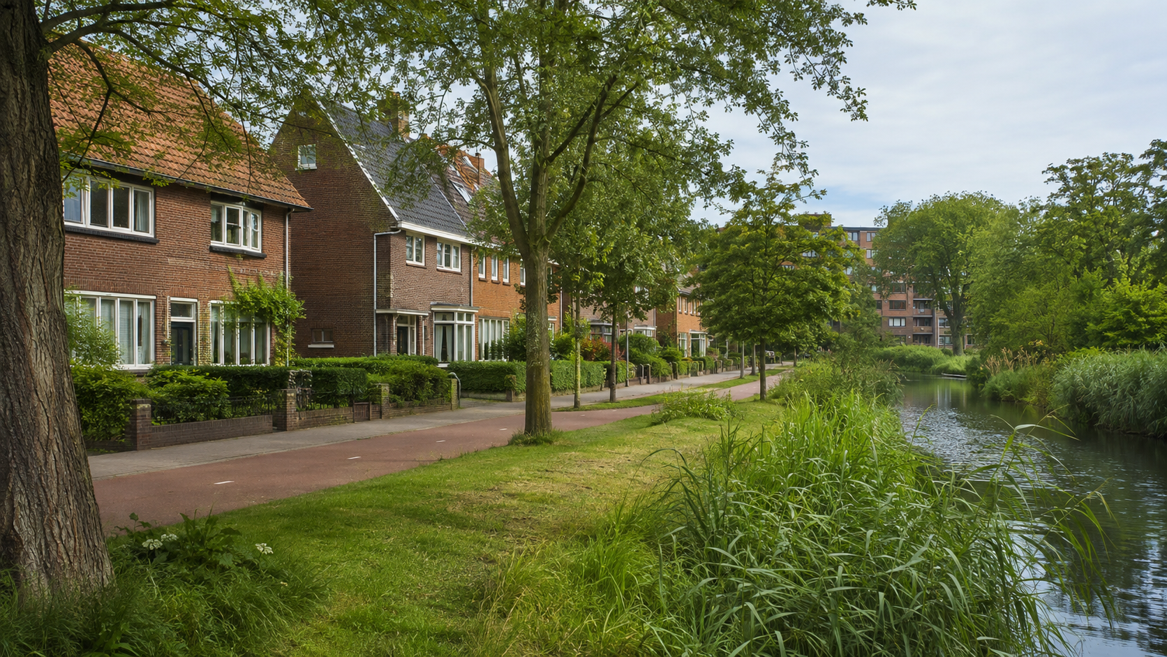 Bakstenen woningen, een groene watergang en bomen in Eindhoven Tongelre